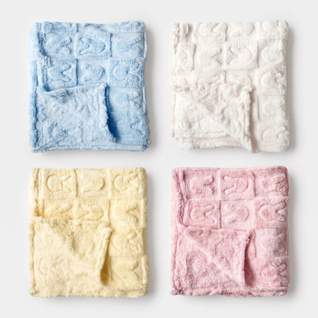 Four plush textured baby blankets in light blue, cream, pale yellow, and dusty pink, arranged in a neat 2x2 grid on a clean white background.
