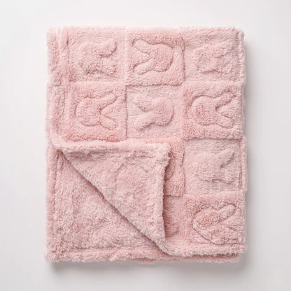 A soft pink plush blanket with a grid pattern of raised square panels, shown folded with one corner turned over on a light gray background.