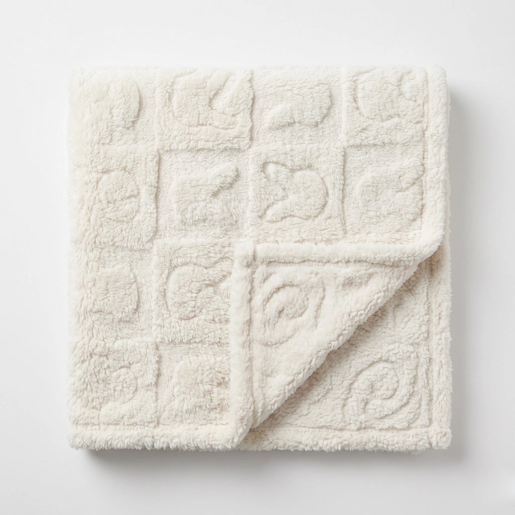 A square cream-colored plush blanket with a quilted grid pattern of raised square motifs, shown folded over on a clean white background.