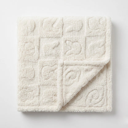 A square cream-colored plush blanket with a quilted grid pattern of raised square motifs, shown folded over on a clean white background.