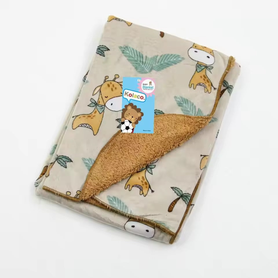 A cozy beige baby blanket, adorned with a giraffe motif and playful leaves, features a soft brown fleece lining from one corner. A blue tag with a lion and soccer ball design adds character, showcasing the brand "Alaya Junior." Product: Cozy Polyester Fleece Plush Velvet Baby Blanket (Giraffe Design).