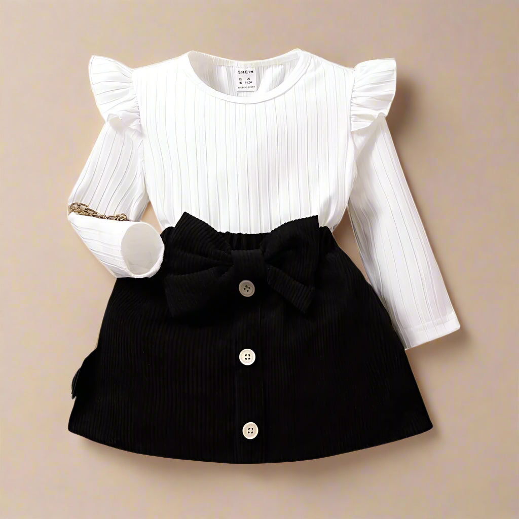 The SHEIN Baby Girl Ruffle Trim Tee & Bow Front Skirt set features a white long-sleeve top and buttoned bow front skirt, styled elegantly on a neutral background.