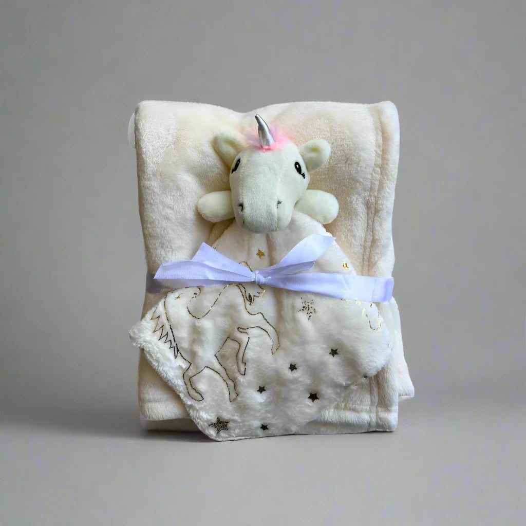 A soft, cream-colored "Soft Baby Blanket with Unicorn Plush Toy" by Alaya Junior is shown, folded neatly with a plush unicorn head at the top. The blanket features star and unicorn patterns, along with a delightful lion pattern, and is tied with a white ribbon.