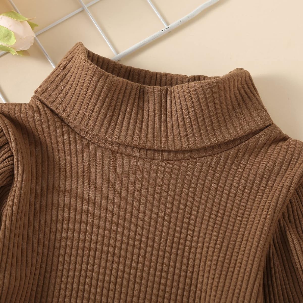 Close-up of a brown ribbed sweater with a turtleneck on a neutral background.