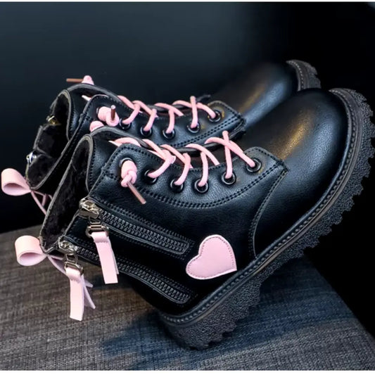 SHEIN's Toddler Girls Long Boots – Stylish Black and Pink with Double Zipper, feature heart embellishments, pink laces, double zippers, pink pull tabs, and a thick sole. These fashionable shoes rest on a dark surface, ready to make a statement.