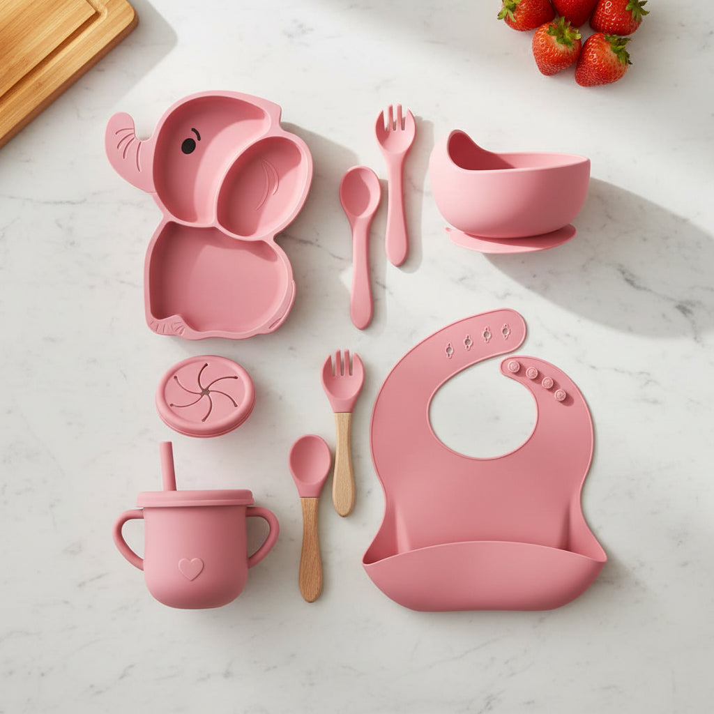 Pink baby utensil set including elephant-shaped spoon, bowl, cup, and bib on a white background