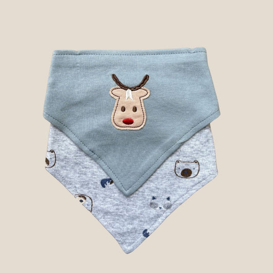 A pair of baby bibs from Alaya Junior, made with ultra-soft cotton, are displayed on a flat surface. The top bib in the set is light blue and features an embroidered reindeer face, while the bottom one is gray with a playful print of bears and foxes. Both bibs come with adjustable snap buttons for convenient use.