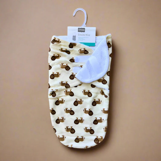 A Lion-Print Winter Swaddle Wrap for Babies by Alaya Junior, designed for comfort during the colder months, features a charming lion pattern and is displayed on a hook against a beige background. The swaddle, crafted from plush fabric with a soft white interior lining, has its label positioned at the top.