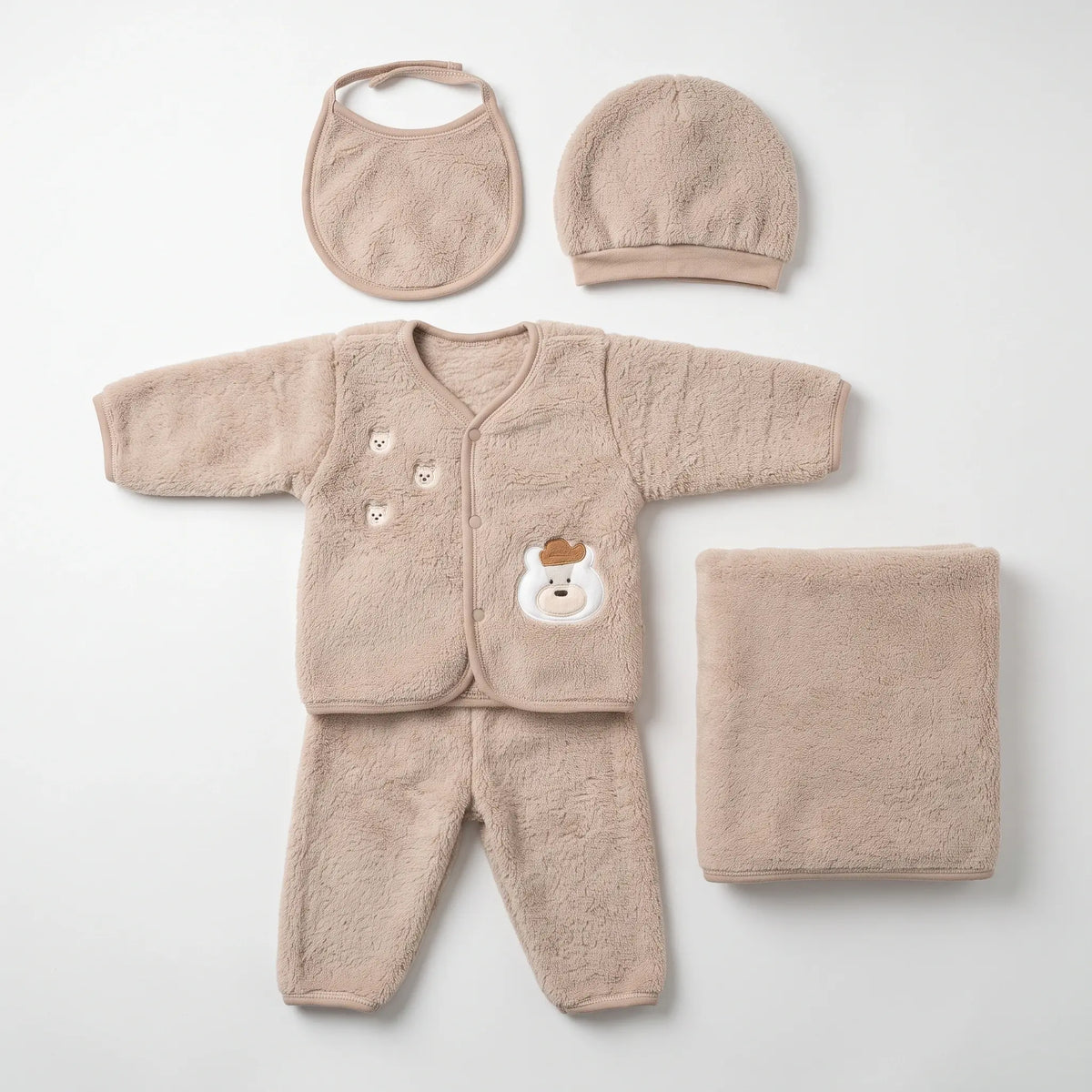 A soft baby clothing set laid flat on a light gray background, including a long-sleeve footless cardigan with a bear face patch, matching pants, a bib, a bonnet, and a folded blanket in a warm beige/tan plush fabric.