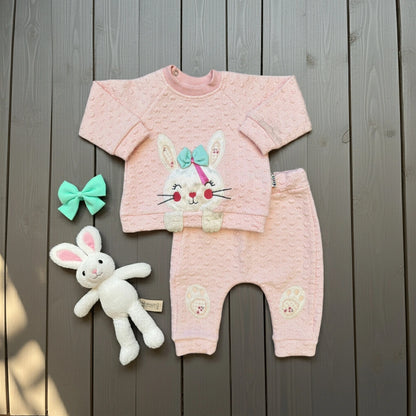Pink baby outfit with bunny design on a wooden surface
