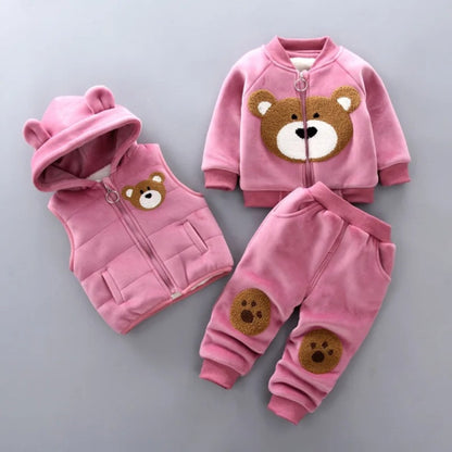 The Alaya Junior Warm Pink Furry Bear Fleece 3-Piece Set for Baby Girls includes ultra-soft fleece children's clothing featuring adorable bear designs: a hooded vest with bear ears and a face on the chest, a long-sleeve jacket with a larger bear face, and matching pants with bear paw prints on the knees.