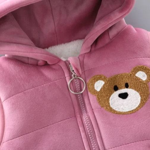 A close-up of the Alaya Junior Warm Pink Furry Bear Fleece 3-Piece Set for Baby Girls showcases a hooded jacket adorned with a ring zipper pull and an adorable teddy bear face patch on the chest. The ultra-soft fleece inner lining adds to its cozy appearance.