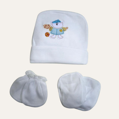 The Adorable White Newborn Cap, Mittens, and Booties Set - Little Theme Unisex Delight from Alaya Junior includes a charming beanie hat featuring an embroidered teddy bear in a blue outfit, alongside cozy mittens and booties. Perfect for newborns, these high-quality infant clothing items are beautifully arranged on a plain, light background, exemplifying the exceptional craftsmanship common in Pakistani baby apparel.