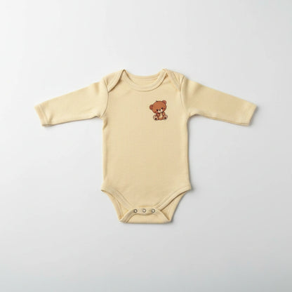 A long-sleeve baby bodysuit in a soft cream-beige color, featuring a small embroidered brown teddy bear on the left chest and three silver snap buttons at the crotch, laid flat on a light gray background.