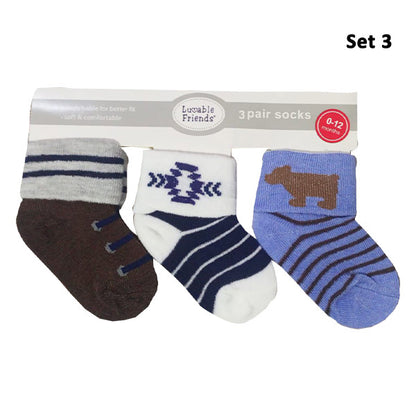 Introducing the Luvable Baby 3-Pair Socks Gift Set by Hudson, designed for ages 0-12 months. This gift set features a stay-on design and includes brown socks with gray stripes, white socks with a navy blue geometric pattern, and blue socks with a brown dog and navy blue stripes. The label reads "3 pair socks.