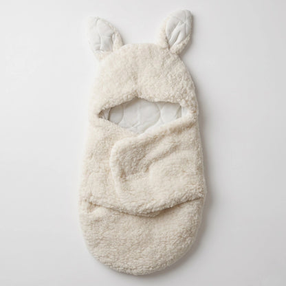 A cream-colored, plush fleece baby bootie with integrated bunny ears, shown flat on a light gray background.