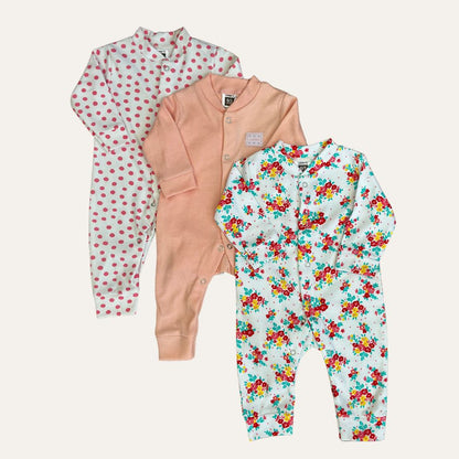 Three adorable baby onesies are displayed, all under the product name "Carters Pack Of 3 Open Feet Romper (Pink Color)" by Alaya Junior. The first one has a white background with pink polka dots, the second is a plain peach color, and the third features a light blue background with a colorful floral pattern. Perfect choices for newborn baby clothing in Pakistan.