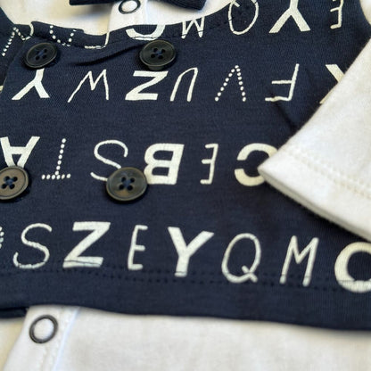 Close-up of a newborn baby wearing the "7pcs Chicco Bow Romper Starter Set with Petite Waistcoat" by Alaya Junior, showcasing a dark blue shirt adorned with white alphabet letters. This trendy baby clothing in Pakistan features four black buttons in a double-breasted design, along with a small collar. The sleeves and bottom edge of the shirt are white.