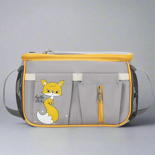 The Alaya Junior Diaper Bag + Stroller Organizer with Charging Cable is a multi-functional travel solution in gray with yellow accents and multiple pockets. The front features a cute cartoon fox and "hello SPRING" text. Made from water-repellent material, it includes a zippered main compartment, mesh side pockets, and exterior pockets for easy organization, balancing practicality and style effortlessly.