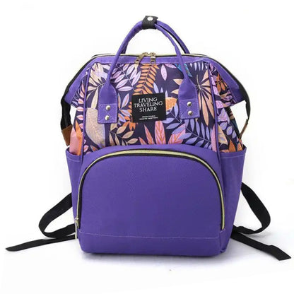 Introducing the Blossom & Bloom Diaper Delight by Alaya Junior, a purple backpack adorned with a floral pattern in shades of pink, orange, and cream on the upper part. This stylish bag features a front zippered pocket, two side pockets, and a top handle, along with black shoulder straps for comfortable carrying. The label on the front reads "LIVING TRAVELING SHARE." It's perfect for transporting infant clothing from Pakistan.