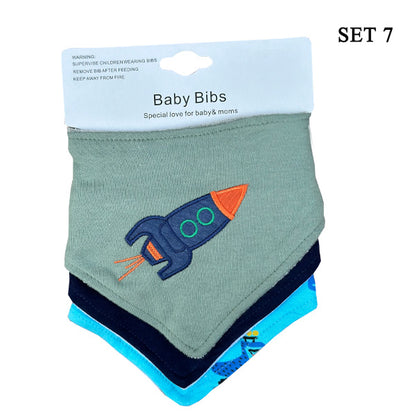 A set of three Alaya Junior Organic Baby Bandana Drool Bibs, made from 100% cotton and designed for ages 0 to 3 years, is displayed against a white background. The top bib features a light gray color with an embroidered rocket ship design, perfect for a newborn baby. Below it, two more bibs in dark blue and light blue are partially visible. The packaging label reads "Baby Bibs" and "SET 7".