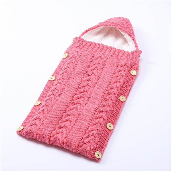 Introducing the Alaya Junior Newborn Baby Sleeping Bag with Sherpa Lining-(0-7 Months), a pink knitted sleeping bag for babies featuring a hood and wooden buttons along the sides. This cozy newborn wrap showcases a cable knit pattern and includes a soft, white sherpa lining inside for extra comfort. Adjustable Velcro closures ensure a snug fit for your little one.