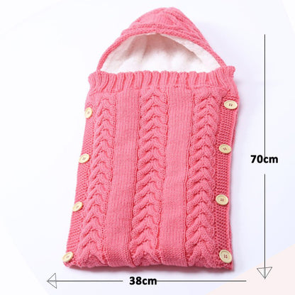 The Alaya Junior Newborn Baby Sleeping Bag with Sherpa Lining (0-7 Months) is a cozy pink, knitted baby sleeping bag featuring a hood. It boasts a charming cable-knit pattern and secures with wooden buttons on the side. This snug newborn baby wrap measures 70 cm in height and 38 cm in width.