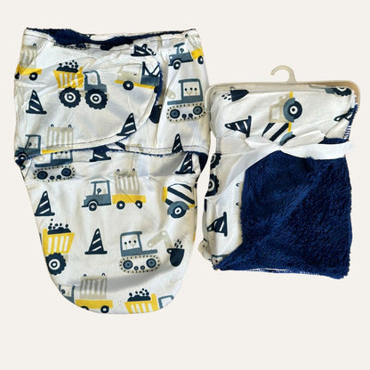 Two white baby blankets from the Cuddly Duo: Baby Winter Blanket with Swaddle collection by Alaya Junior, featuring adorable construction vehicle patterns in yellow, blue, and black tones. One blanket is unwrapped to display its full design, while the other is folded and wrapped with a white ribbon, highlighting its soft navy blue lining. Perfect for newborns in Pakistan, these blankets are essential baby clothing items.