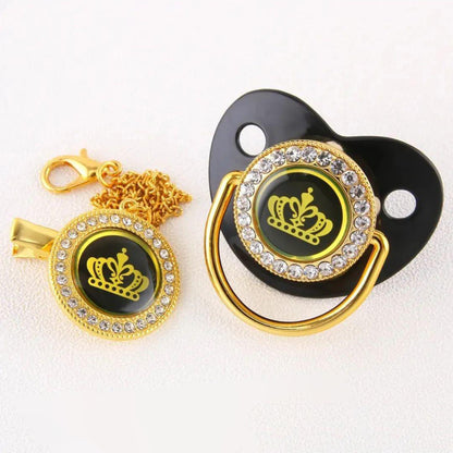 The alayajunior BPA Free Pacifier for Baby with chain is beautifully designed with a black base adorned by a gold rim and jewel-like accents. It features a yellow crown design at the center, making it perfect for a newborn baby. The set includes a matching gold chain clip that also showcases the elegant crown design bordered by jewel-like accents, making it ideal for attaching to baby clothing in Pakistan.